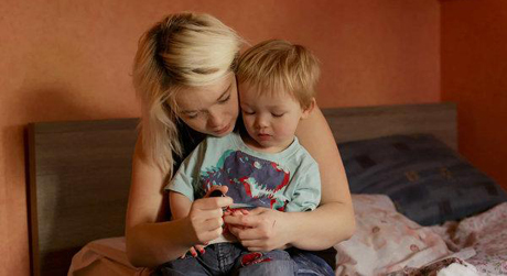 Still from Milla: Milla (played by Séverine) holds her toddler son (played by her real-life son Ethan) on her lap as she sits on a bed.